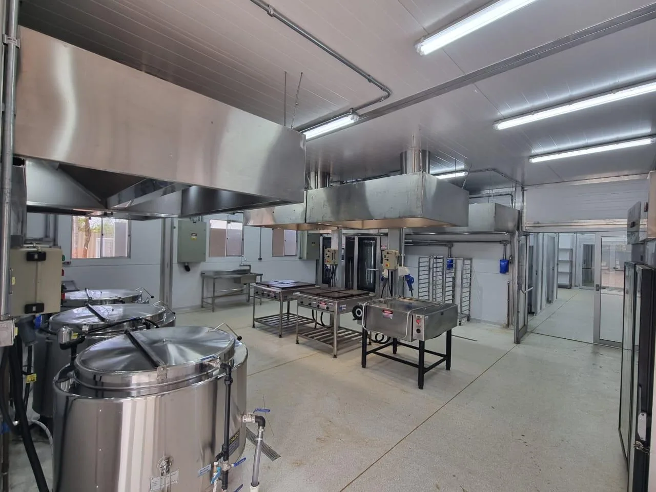Interior de cozinha container Deloc em operação, com caldeirões, coifas de exaustão e bancadas em inox